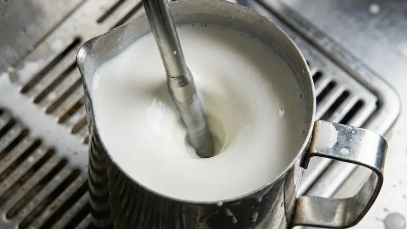 Milk spinning in a powerful vortex inside a stainless steel pitcher, showing the texturing phase where large bubbles are broken into microfoam