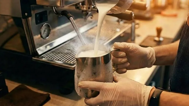 Cold milk being poured into a chilled stainless steel pitcher, showing the starting point for temperature calibration by hand feel
