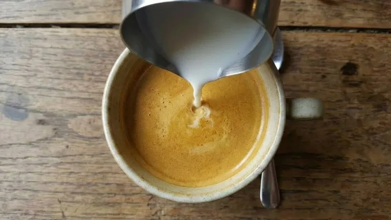 Overhead shot showing the pitcher being lowered slightly as the cup fills, maintaining a centered pour while the crema begins to swirl and prepare for the marking phase