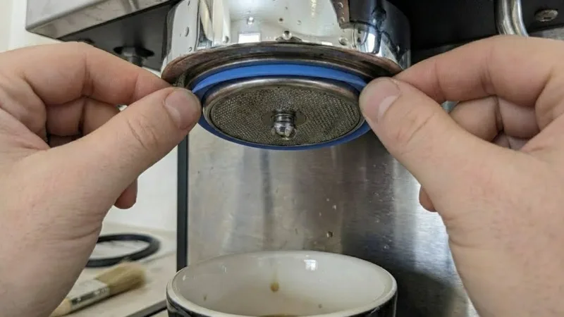 Barista pressing a new blue silicone gasket into the group head groove, ensuring it's seated evenly and ready for the shower screen reassembly